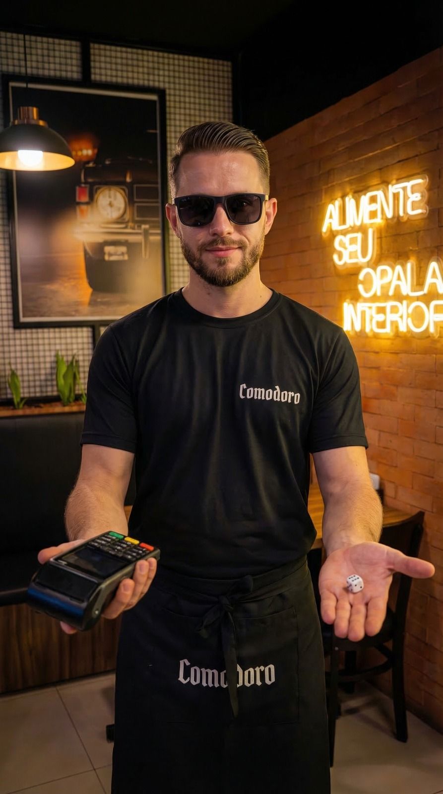 Garçom do Comodoro com a maquininha em uma mão e o dado da sorte na outra