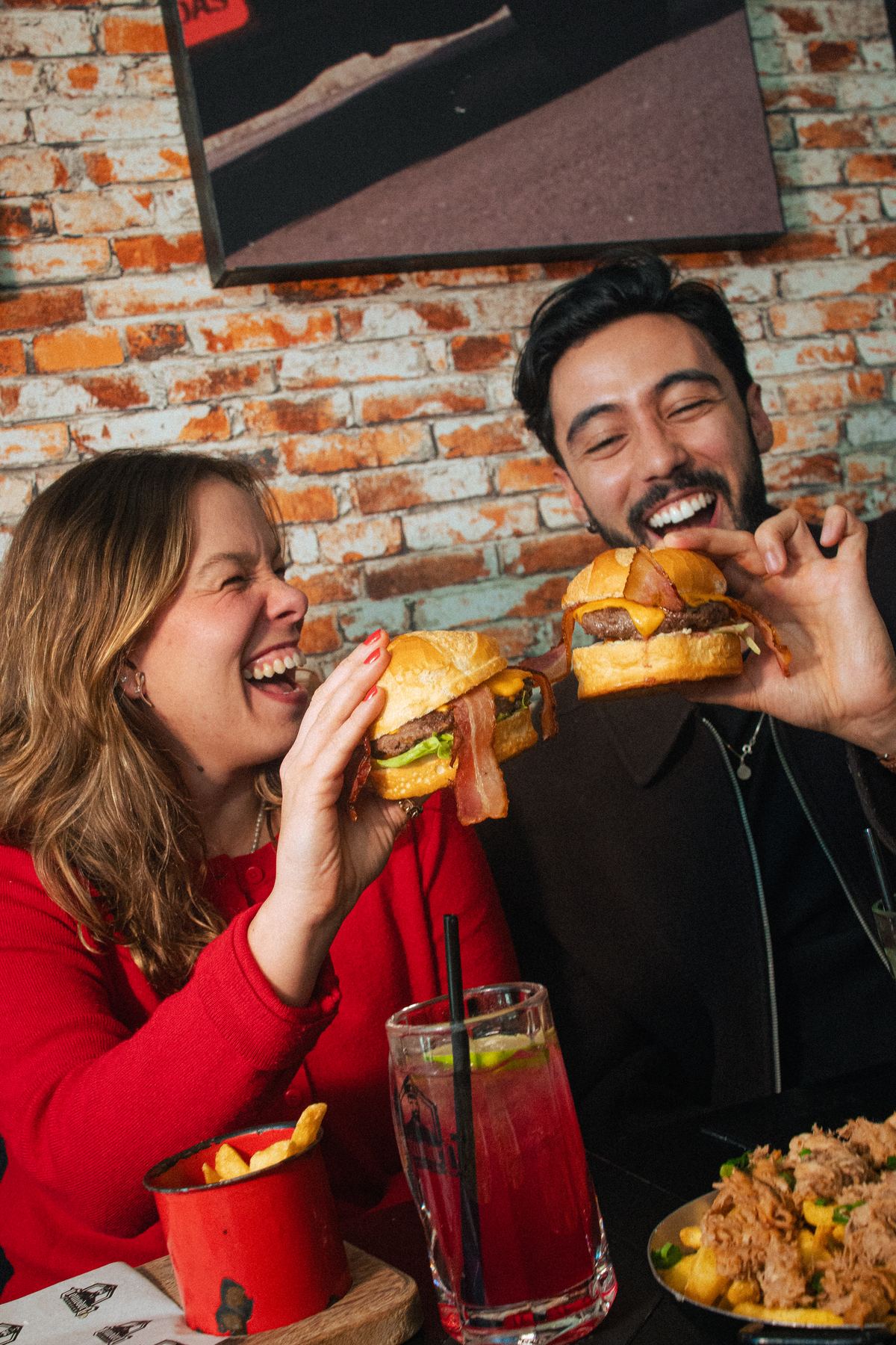 Casal rindo e mordendo o burguer no salão do Comodoro